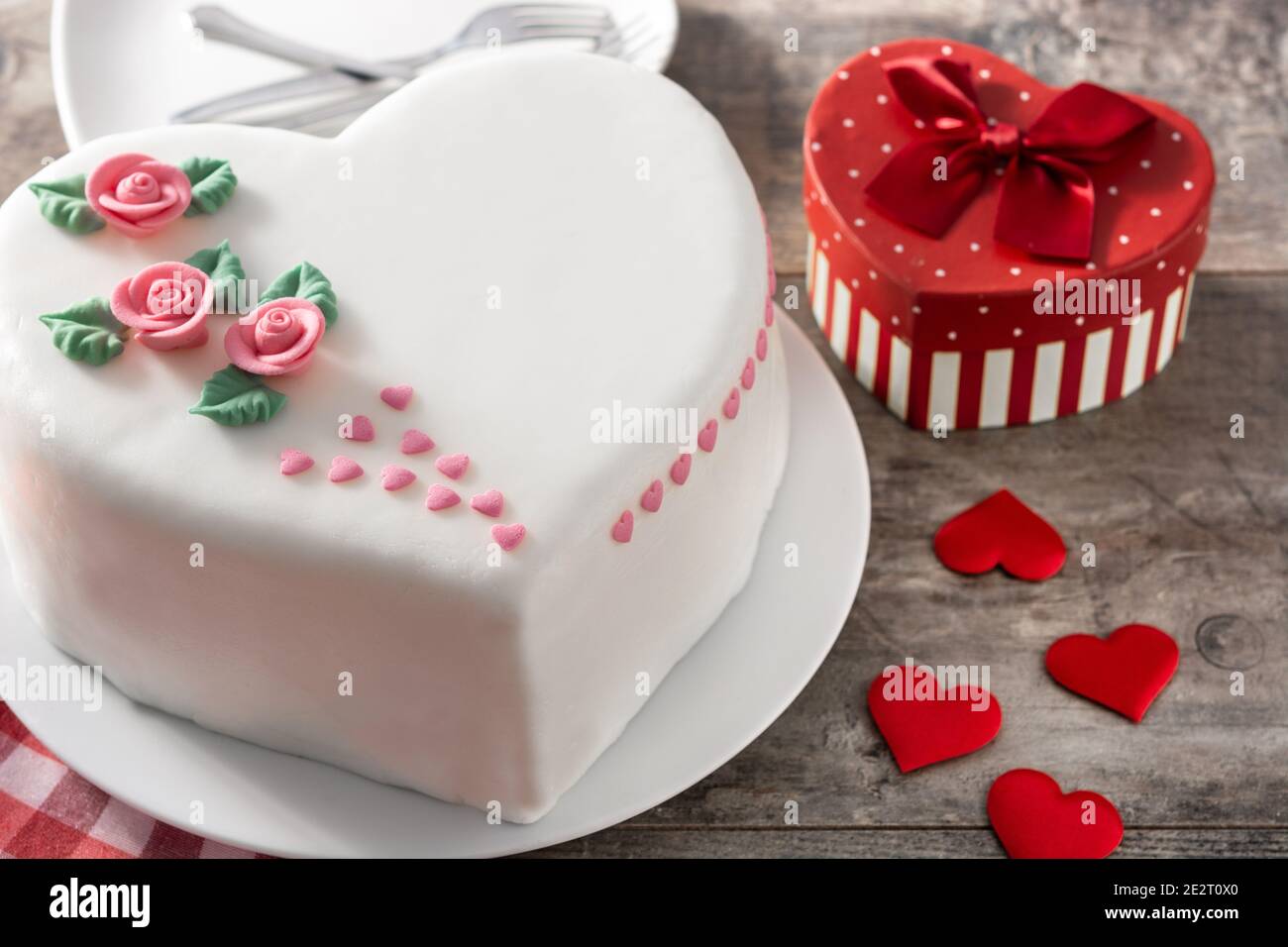 Torta cuore per San Valentino, Festa della mamma o compleanno, decorata con rose e cuori di zucchero rosa su tavola di legno. Foto Stock
