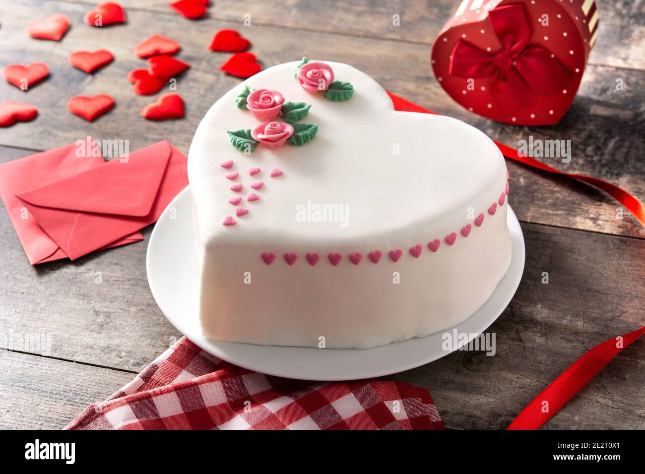 Torta cuore per San Valentino, Festa della mamma o compleanno, decorata con rose e cuori di zucchero rosa su tavola di legno. Foto Stock