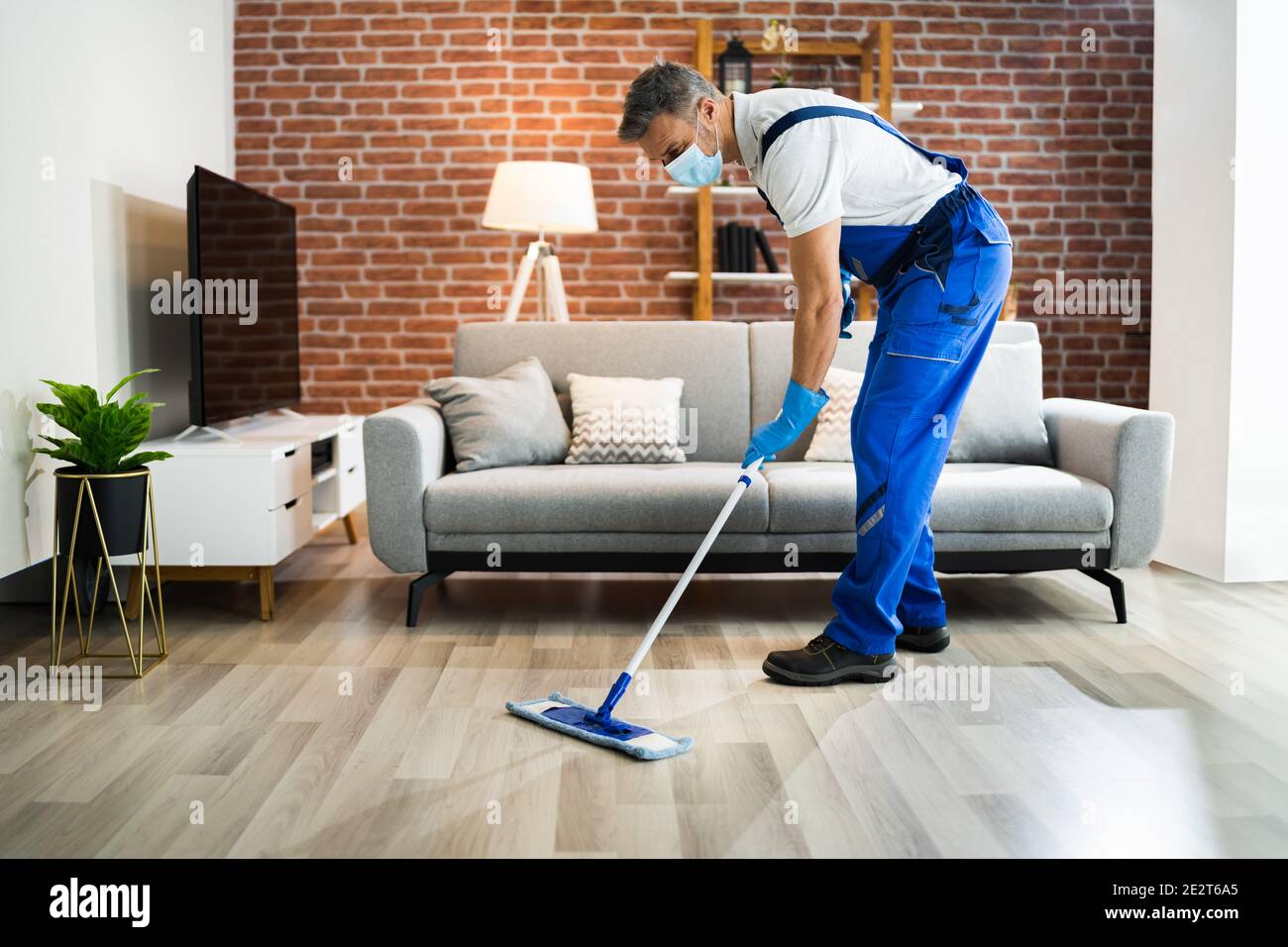 Uomo pulizia del pavimento in legno duro con Mop in maschera facciale Foto Stock