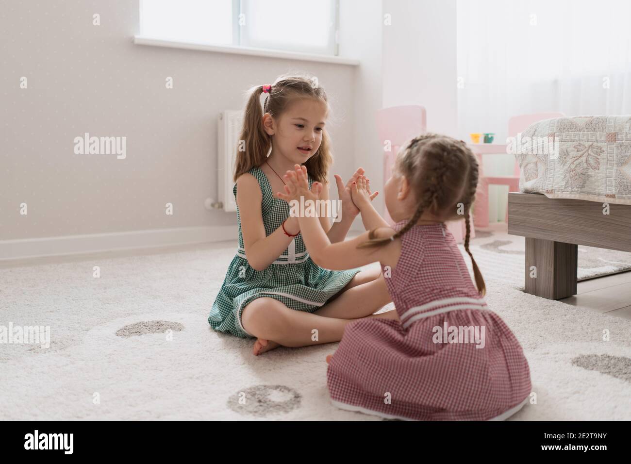 Carine piccole sorelle che giocano insieme seduta sul tappeto in abiti identici colori diversi in una stanza con molta luce Foto Stock