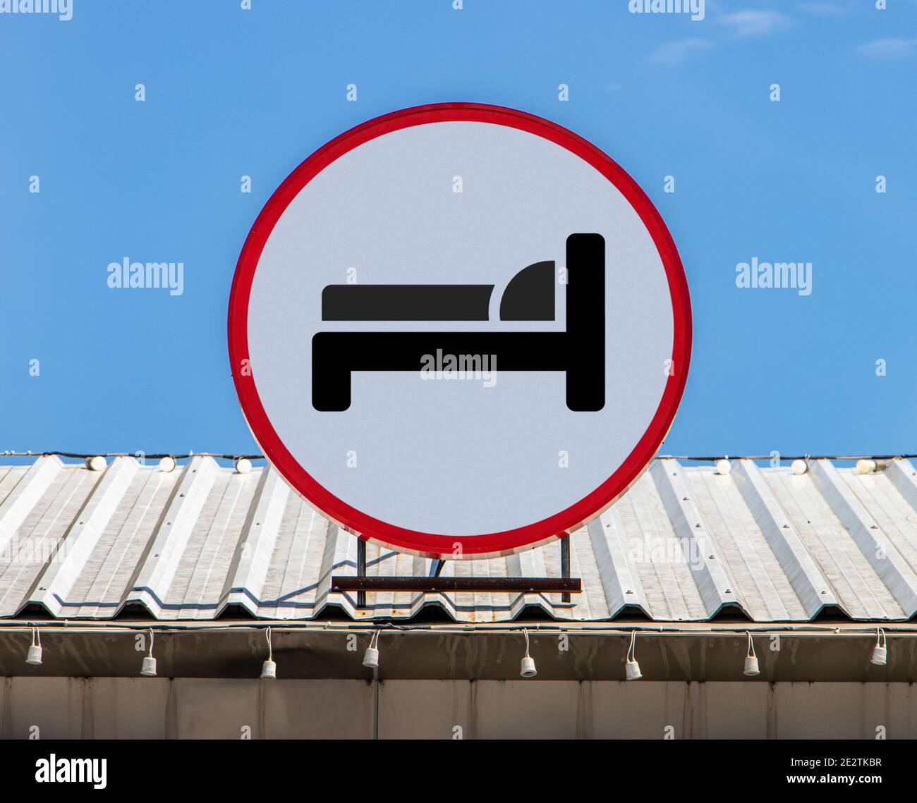 Un cartellone circolare con l'icona una camera da letto simbolo dell'hotel, è installato su un tetto. Sistemazione in ostello. Foto Stock
