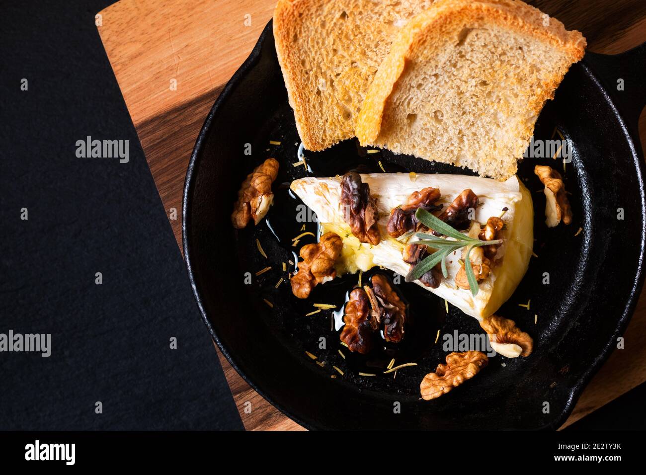 Concetto di cibo punto fuoco casereccio cotto formaggio Brie con miele e noci in padella di ferro su tavola di legno con spazio di copia pietra ardesia nera Foto Stock