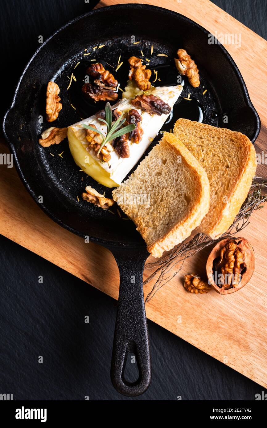 Concetto di cibo punto fuoco casereccio cotto formaggio Brie con miele e noci in padella di ferro su tavola di legno con spazio di copia pietra ardesia nera Foto Stock