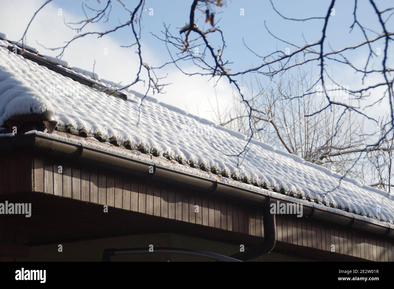Neve sul tetto sotto il sole. Una copertura invernale a strati di tegole coperte bianche dal sole. Bella vista stagionale rurale. Foto Stock
