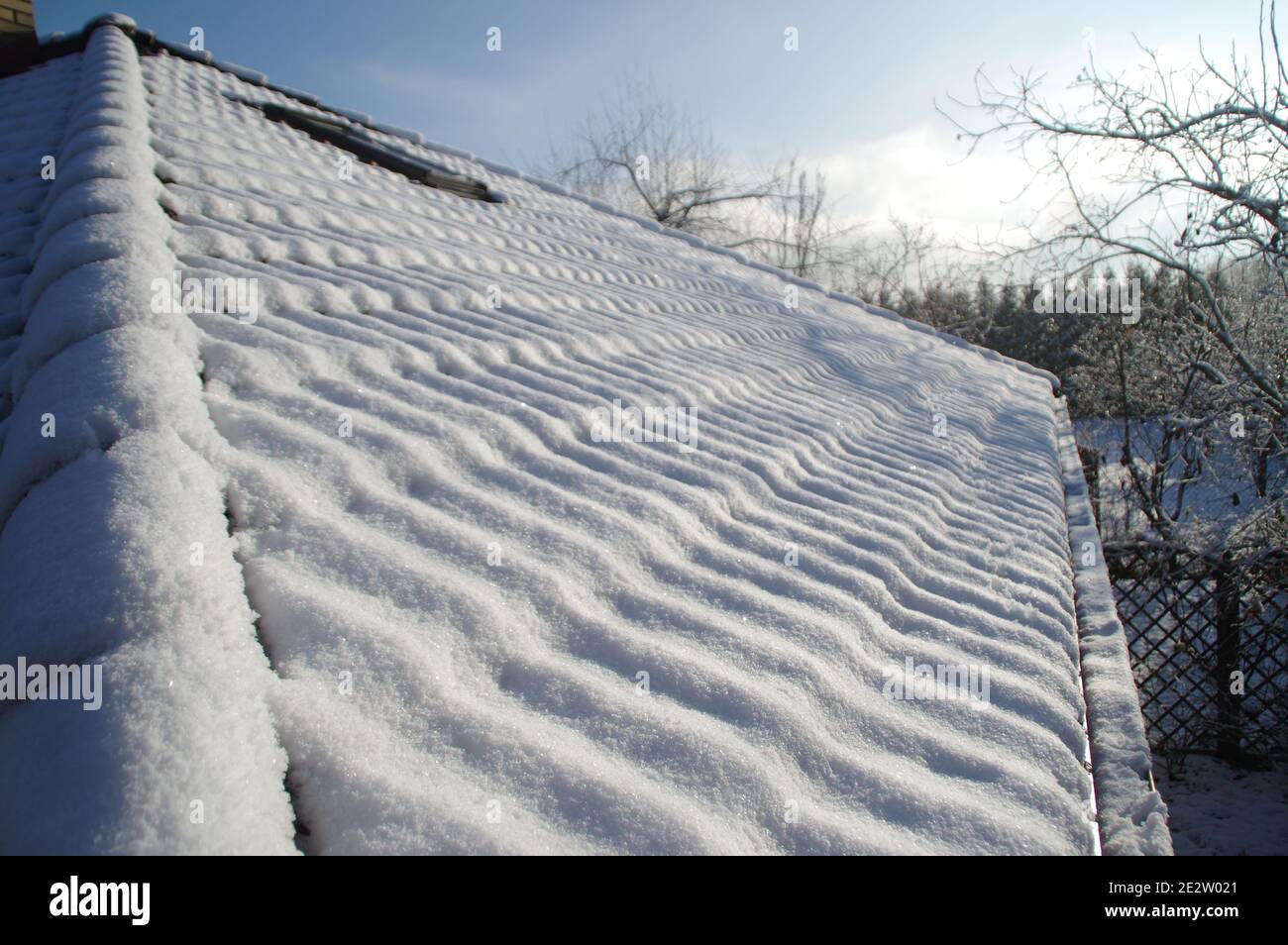 Neve sul tetto sotto il sole. Una copertura invernale a strati di tegole coperte bianche dal sole. Bella vista stagionale rurale. Foto Stock
