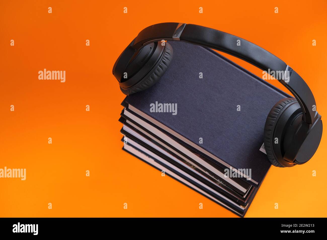 Concetto audiobooks.Reading. Formazione e conoscenza. Formazione a distanza. Una pila di libri e cuffie su sfondo arancione. Audiolibri, e-book Foto Stock