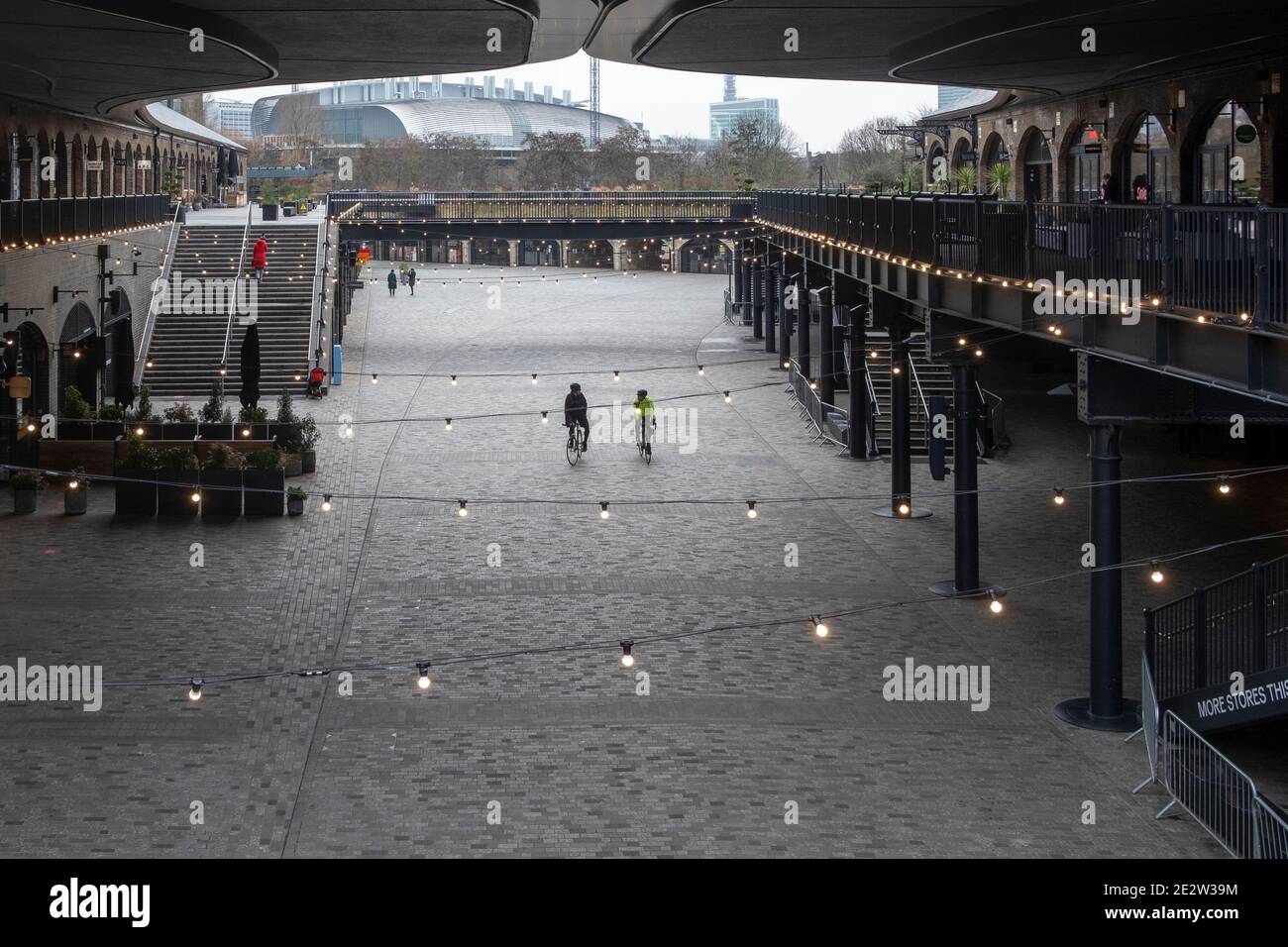 Lockdown London 2021 gennaio: Un paio di ciclisti pedalano attraverso il centro commerciale Coal Drops chiuso, chiuso, chiuso e desertato a Kings Cross, Londra. Foto Stock