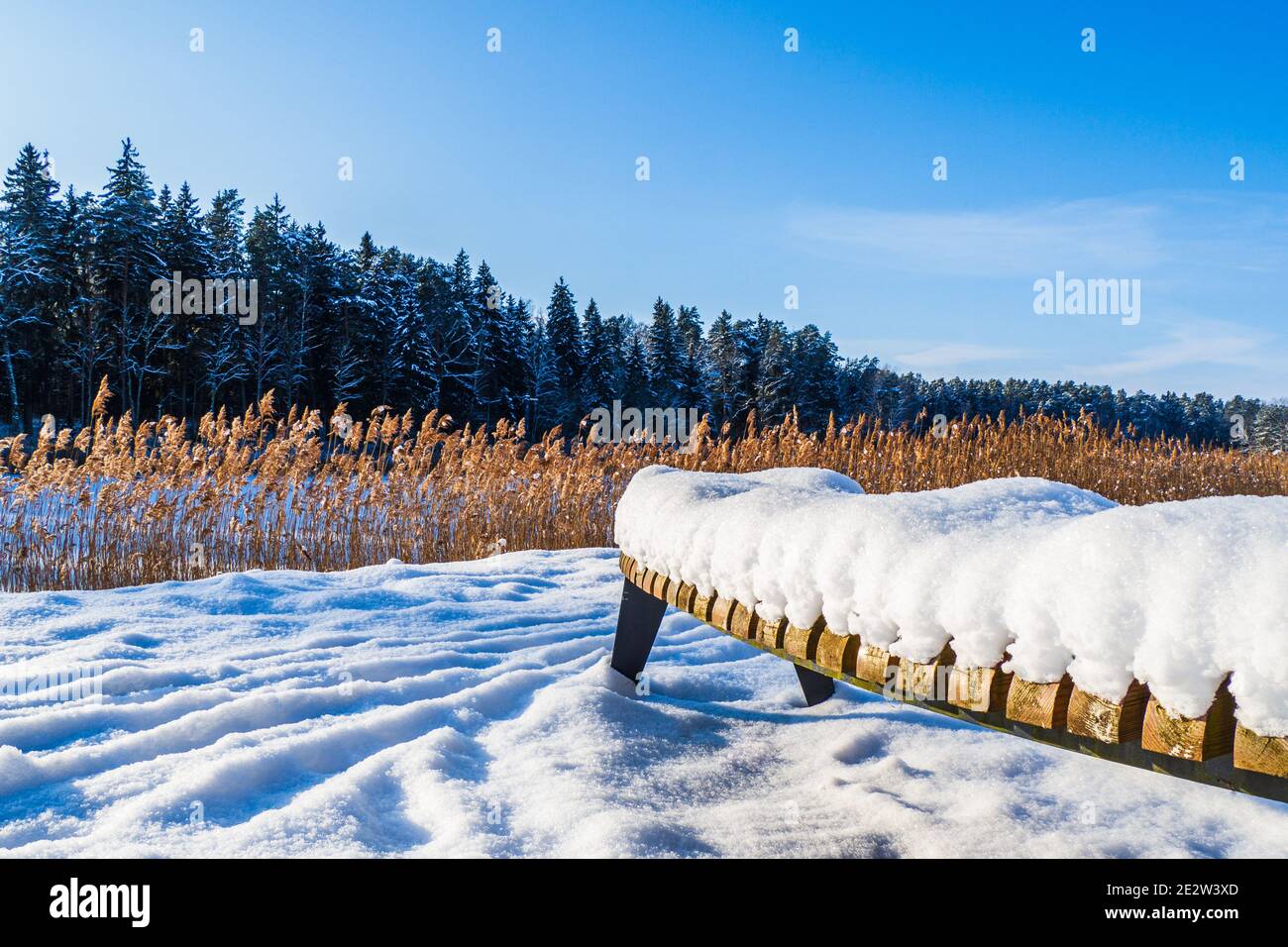 Un banco di legno al bordo di un lago coperto Interamente dalla neve Foto Stock