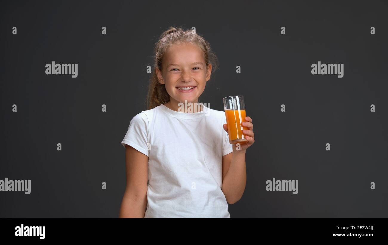 Carina studentessa che tiene un bicchiere di succo d'arancia con una t-shirt bianca sorridente alla macchina fotografica mentre si trova in studio isolato su sfondo nero. Bambini Foto Stock
