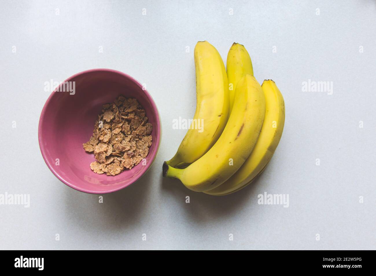 Ciotola rosa con fiocchi di mais e banane gialle, vista dall'alto Foto Stock