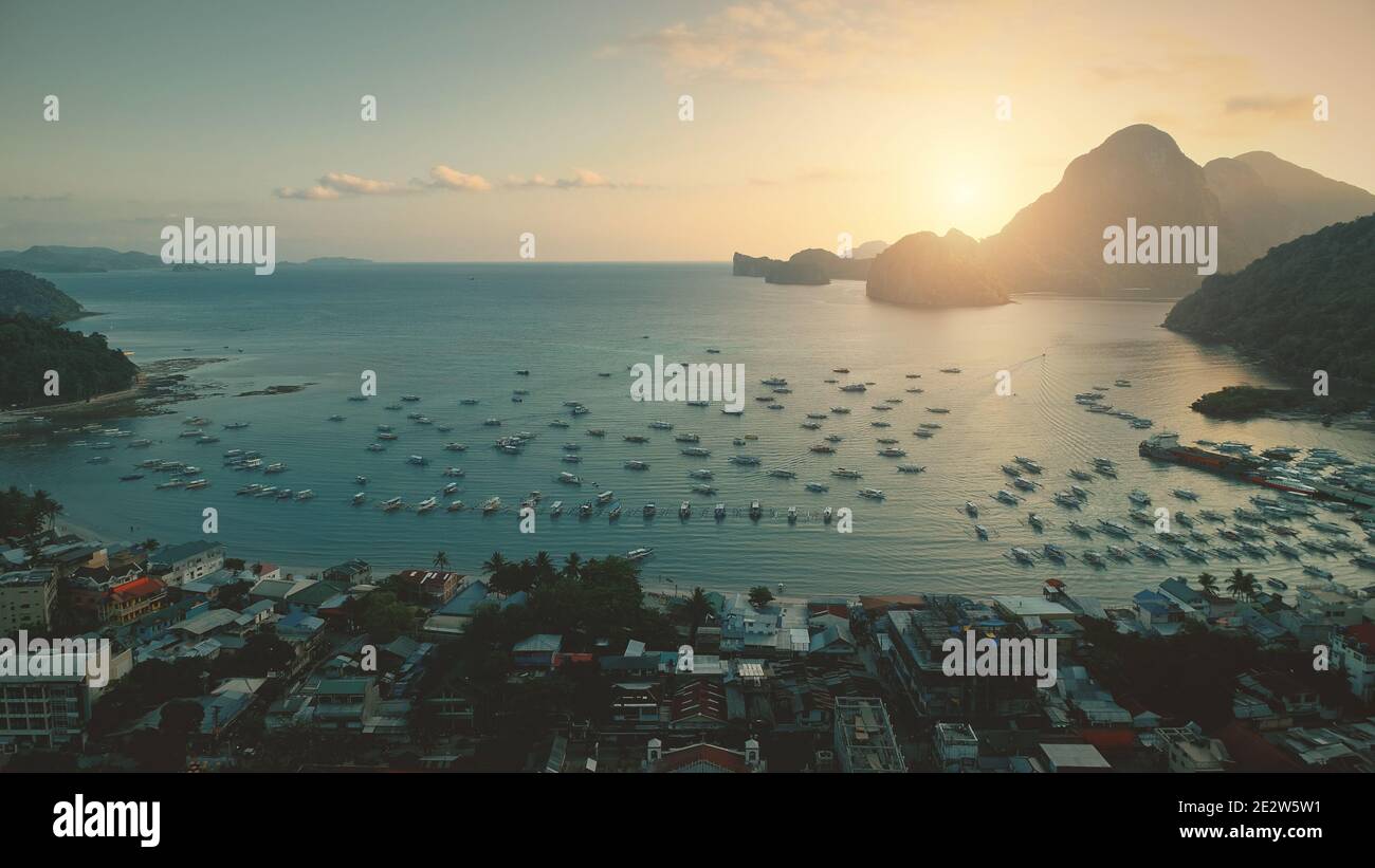 Vista aerea della baia dell'oceano del tramonto al porto con trasporto d'acqua in un paesaggio urbano tropicale. Città paradisiaca delle isole Filippine. Monte verde con alberi di bosco in estate soleggiato giorno. Scatto con drone cinematografico Foto Stock