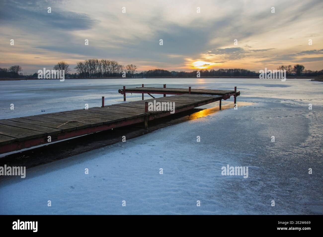 Un lago ghiacciato con un molo, nuvole e tramonto sul cielo, paesaggio invernale Foto Stock