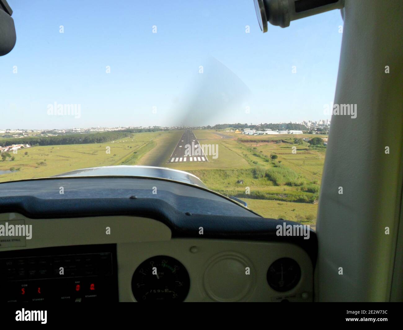 Piccola cabina di aeroplano che si avvicina per l'atterraggio, vista interna, con pista di fronte alle case e all'orizzonte edificio della città, Brasile, Sud Foto Stock