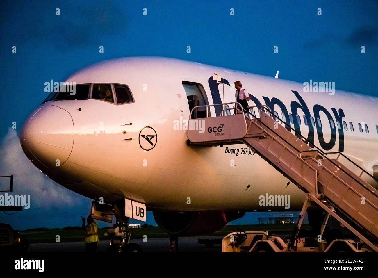 Un Boeing 767-300 della compagnia aerea Condor è fermo all'aeroporto internazionale Grantley Adams vicino a Christ Church, Barbados, mentre un membro dell'equipaggio sale la scala del gestore di terra GCG Groundhandling per imbarcarsi e cala il buio. Foto Stock