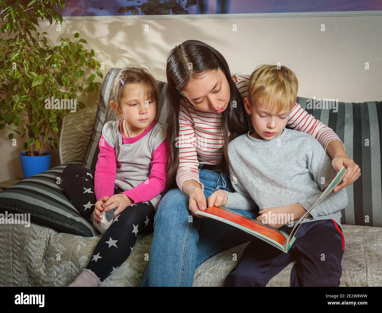Ragazza nanny legge un libro ai bambini. Lavorare con i bambini a casa. Educazione e passatempo con i bambini Foto Stock