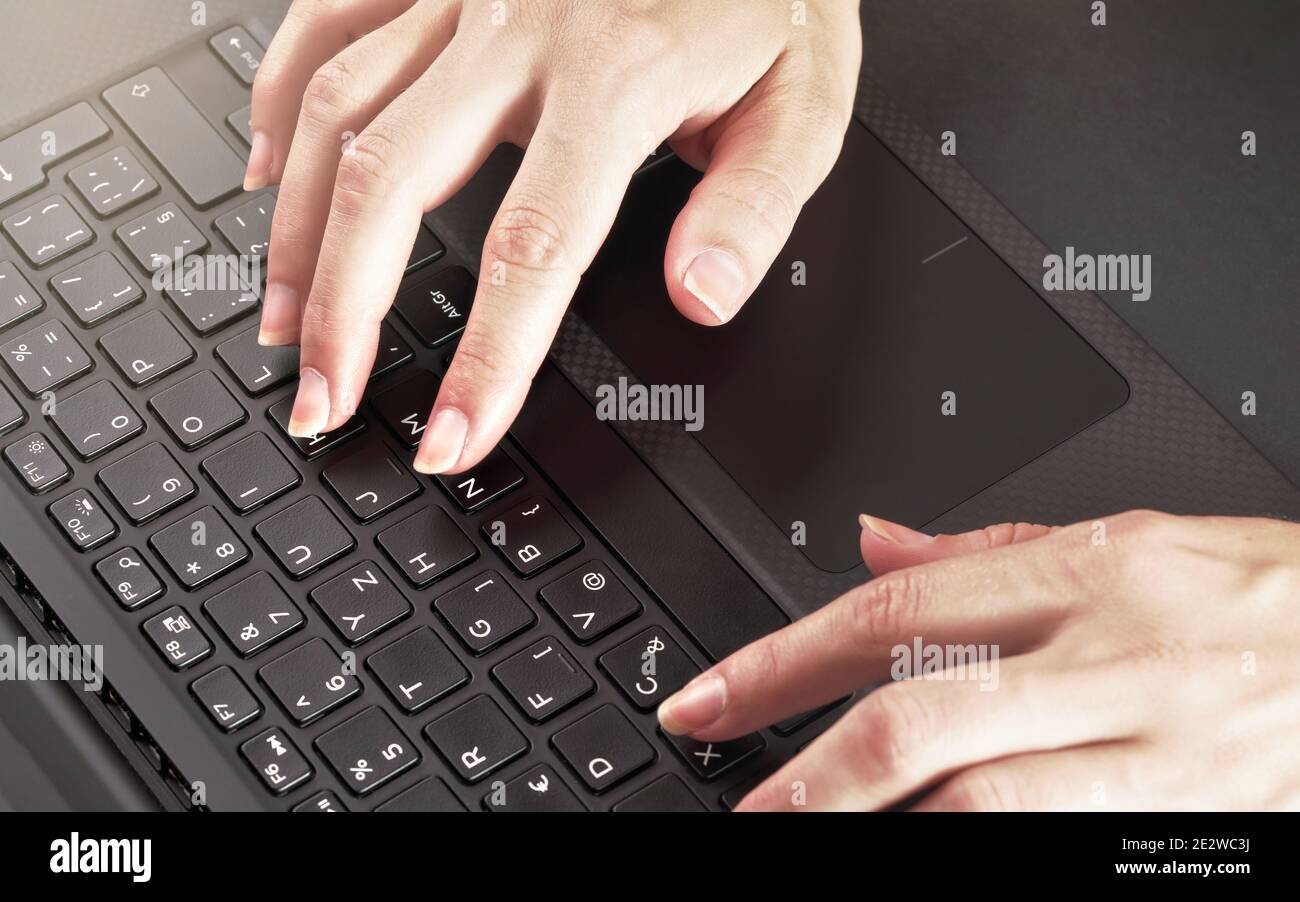 Le mani della donna scrivano sulla tastiera nera del laptop, primo piano dall'alto Foto Stock