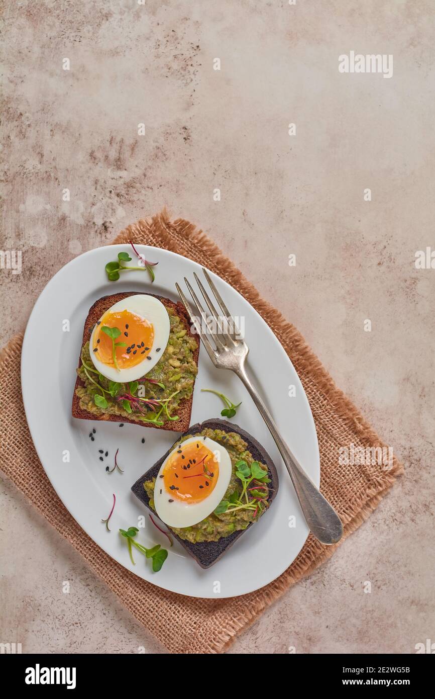 Un sano sandwich con avocado, uova e micrograni su un piatto da portata per la colazione. Concetto dietetico di nutrizione sana. Vista dall'alto. Foto Stock