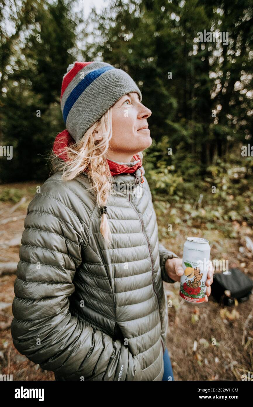 Donna bionda sorridente in giacca grigia e cappello invernale che tiene la birra. Foto Stock