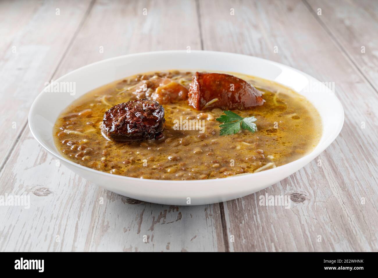 Lenticchie con chorizo, salsiccia di sangue e verdure, in piatto caldo su tavola di legno Foto Stock