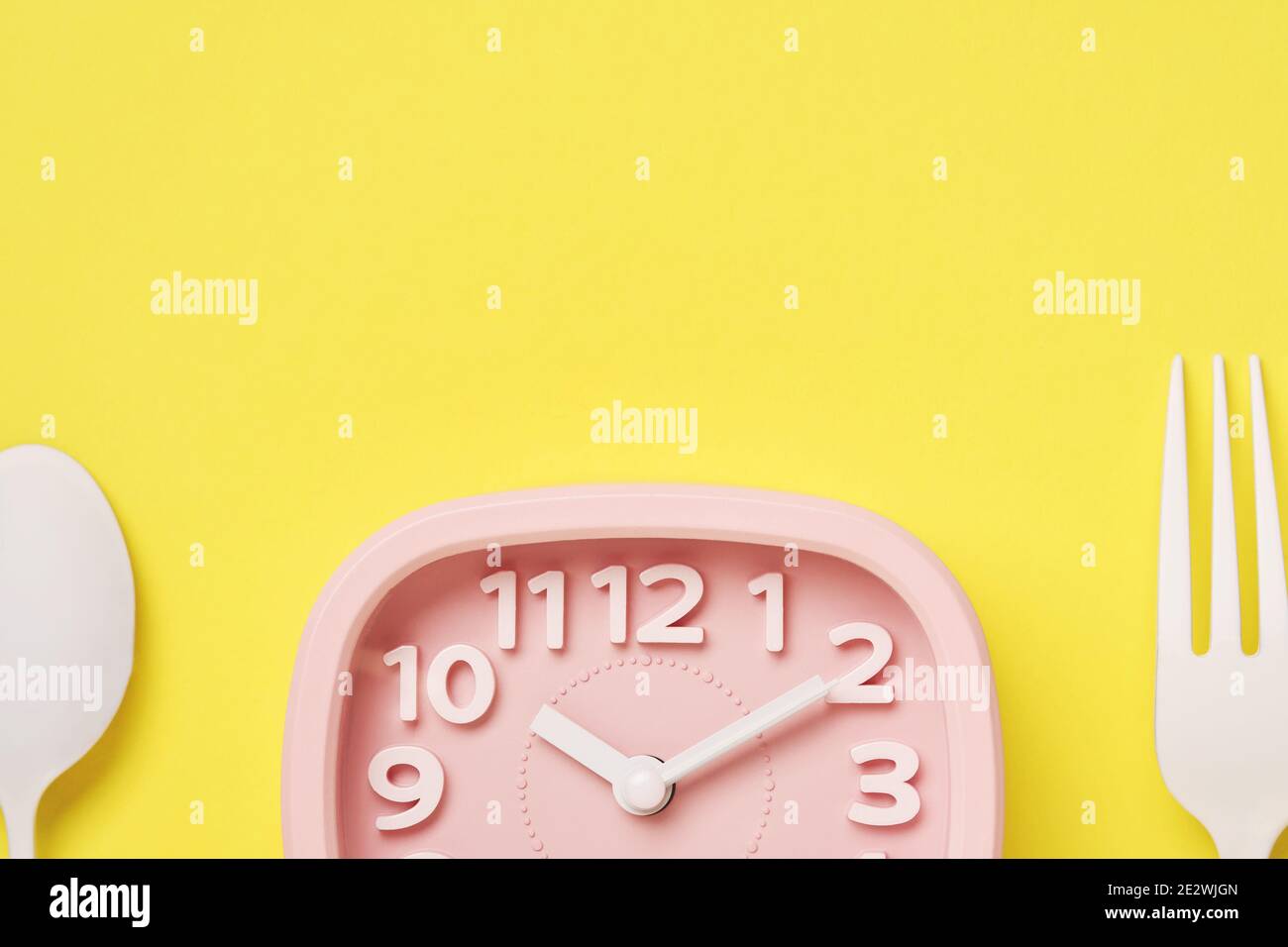 Orologio retro rosa e cucchiaio bianco e forchetta su sfondo giallo con spazio per la copia. Concetto di tempo e dieta. Foto Stock
