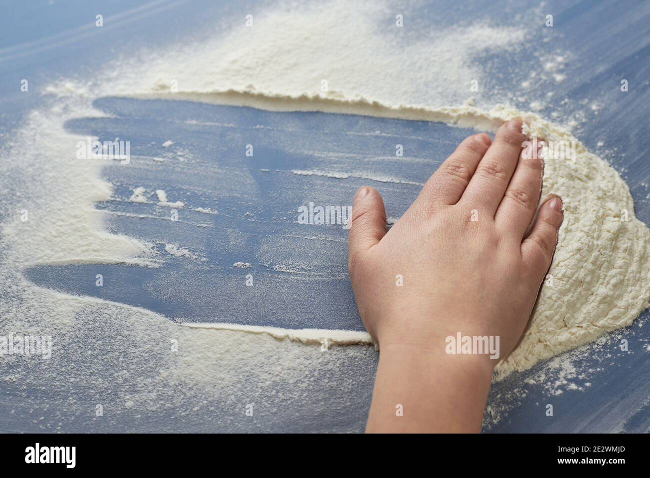 La mano della donna rimuove la farina su sfondo blu, il tema della cucina. Foto Stock