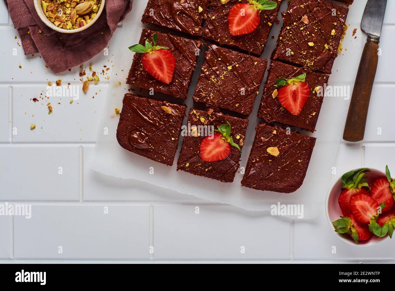 Quadrati di cioccolato con pistacchio e fragole su carta bianca su sfondo chiaro, vista dall'alto, composizione orizzontale. Foto Stock