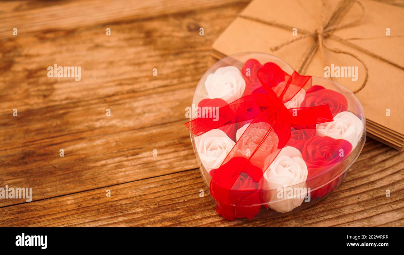 Lettere in buste di carta artigianale e un regalo di rose su sfondo di legno Foto Stock