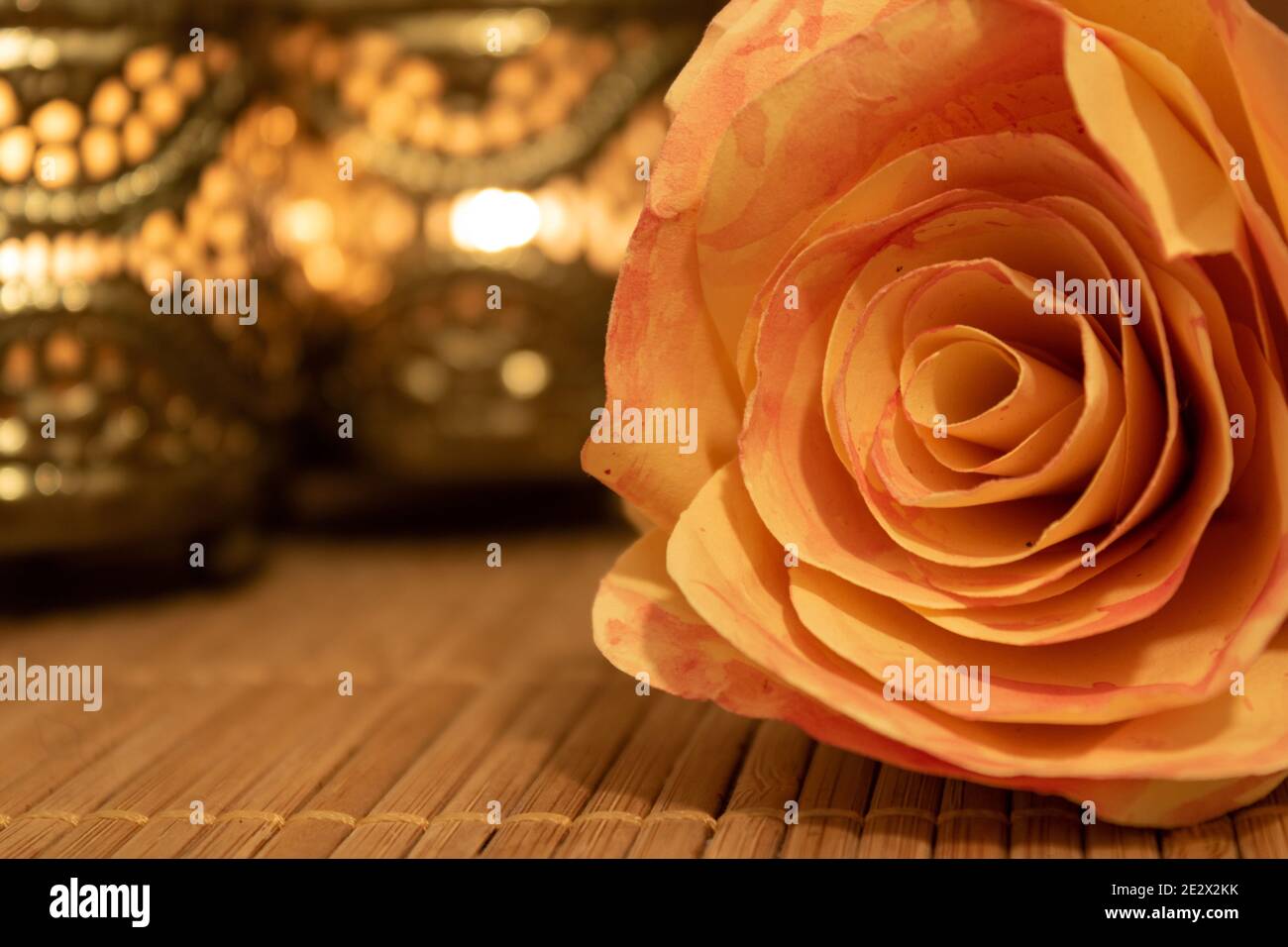 Primo piano di fiori di rosa fatti di carta giacente su tavola di legno con candele ornamentali sfocate sullo sfondo. Concetto di benessere Foto Stock