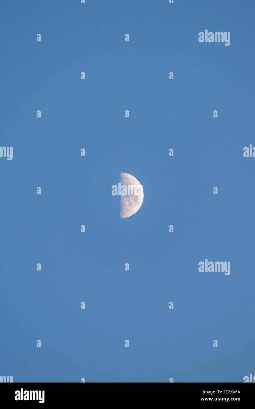 Primo piano di un quarto di luna in un cielo azzurro limpido e senza nuvole al tramonto, Ericeira, Portogallo. Foto Stock