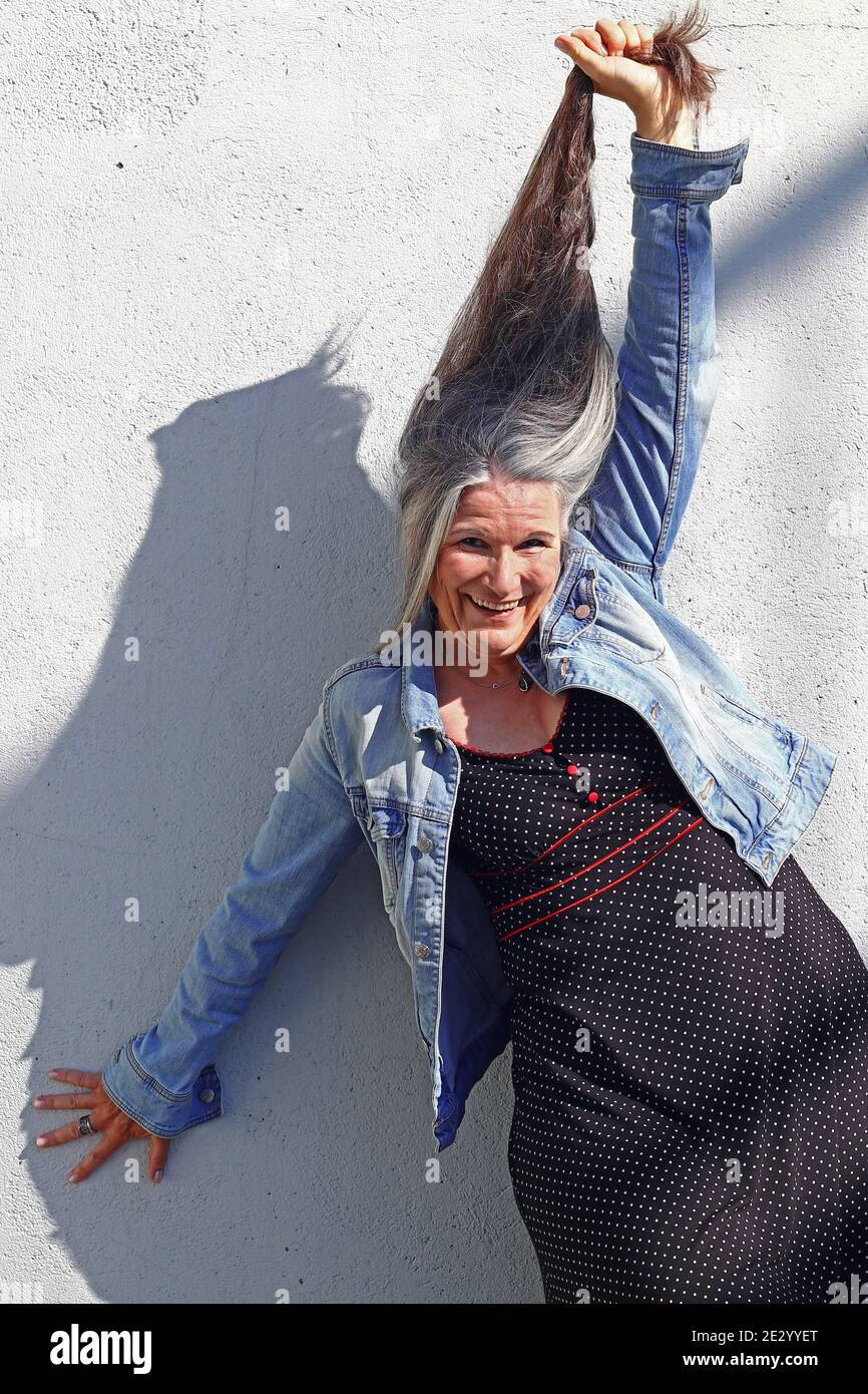 Una donna più anziana che ride allunga i suoi lunghi capelli grigi verso l'alto Foto Stock