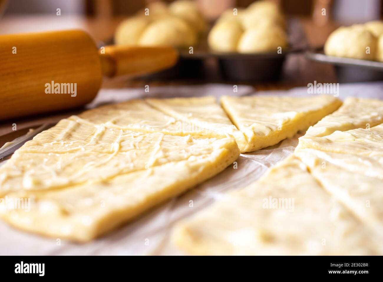 Sfoglia l'impasto di lievito per i rotoli di mezzaluna. L'impasto è stato lathered in burro. Perno di rotolamento in legno sullo sfondo. Pasta su carta pergamena. Ad Foto Stock