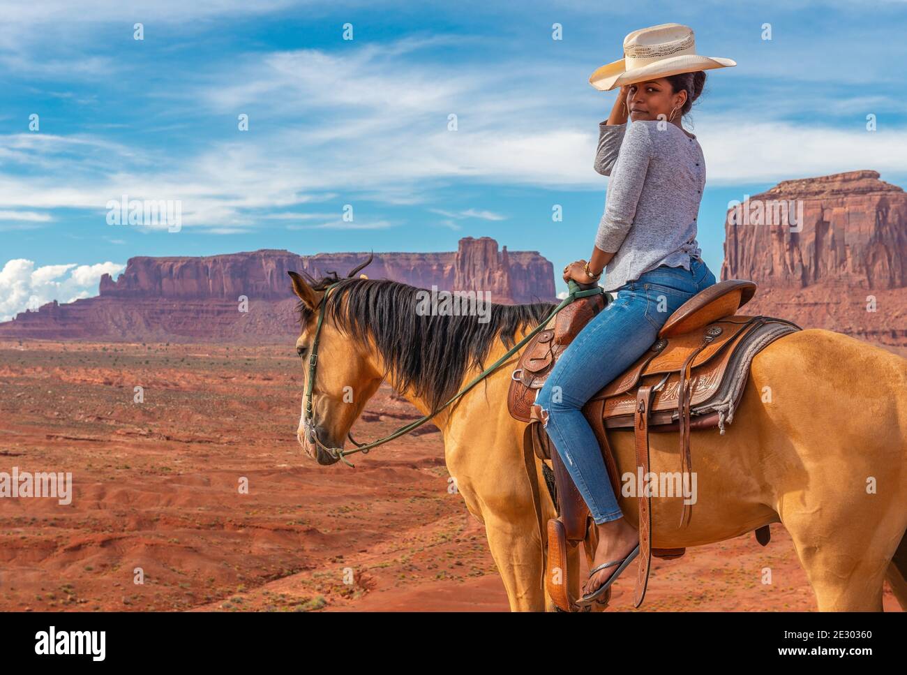 Giovane donna afroamericana a cavallo dal punto di vista di John Ford con West Mitten butte e Mitchell mesa, Monument Valley Navajo Tribal Park, USA. Foto Stock