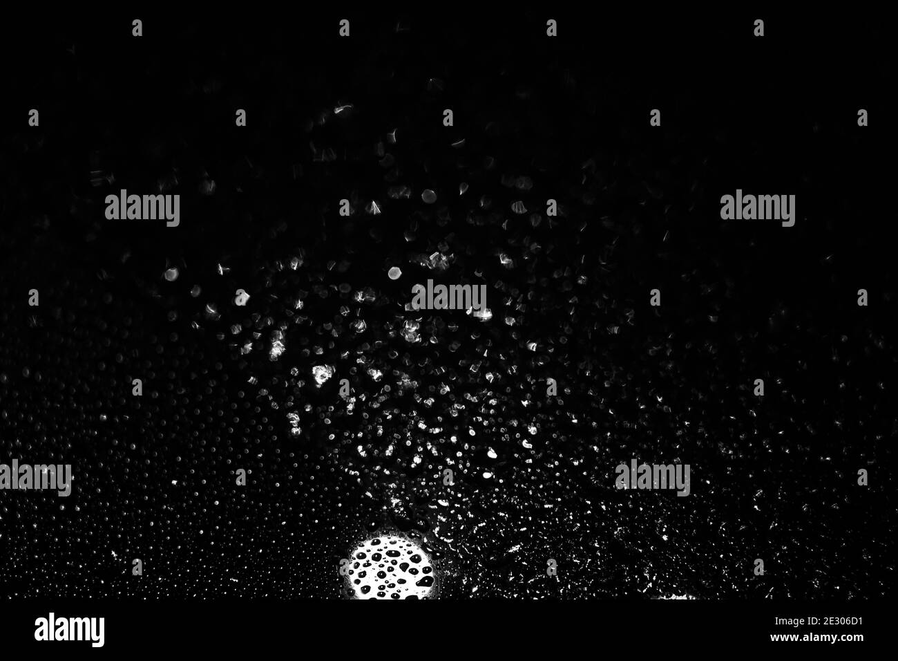gocce di pioggia sul vetro di notte, sfondo scuro, texture in bianco e nero, sfocatura e sfocatura. Foto Stock