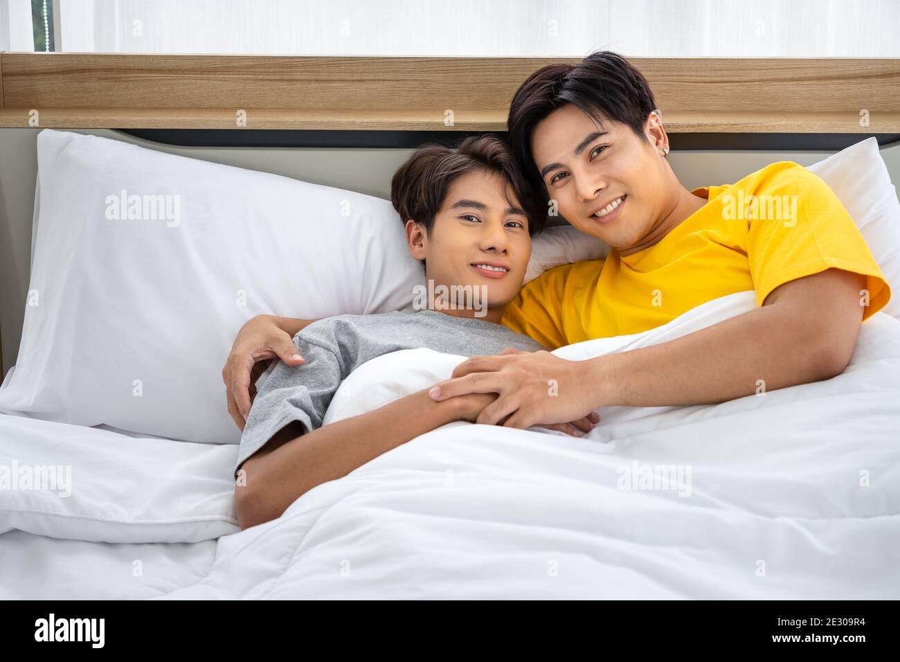 Felice omosessuale asiatico uomini gay coppia maschile mentendo e abbracciando a letto. LGBT e concetto di diversità sessuale. Guardando la fotocamera. Foto Stock