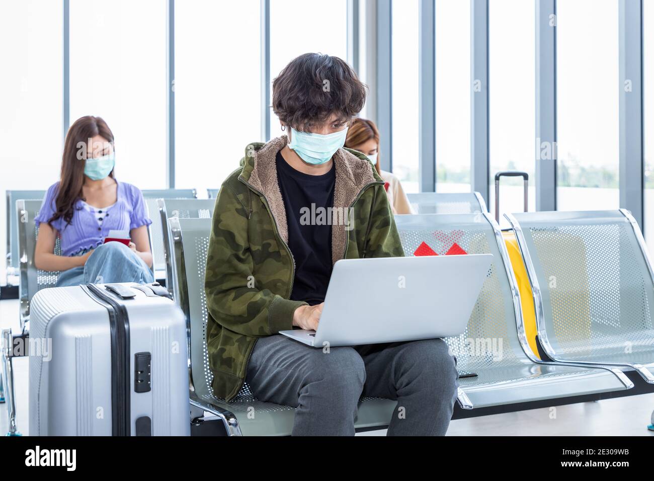 Viaggiatore che indossa una maschera protettiva in aeroporto, durante la pandemia di Covid-19, con protocollo di allontanamento sociale. Utilizzo di un computer portatile durante l'attesa del volo Foto Stock