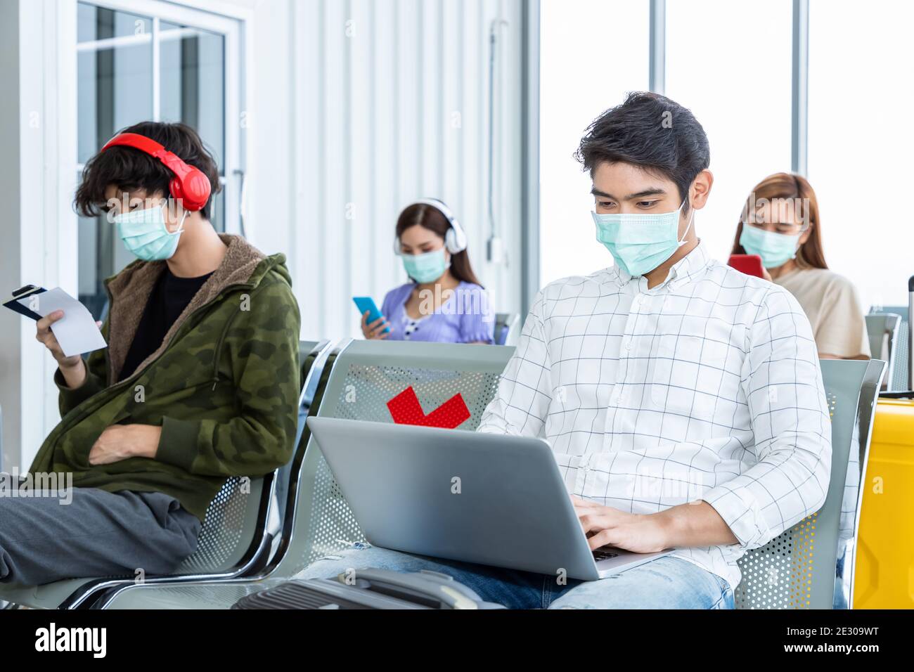 Viaggiatore che indossa una maschera protettiva in aeroporto, durante la pandemia di Covid-19, con protocollo di allontanamento sociale. Utilizzo di un computer portatile durante l'attesa del volo Foto Stock