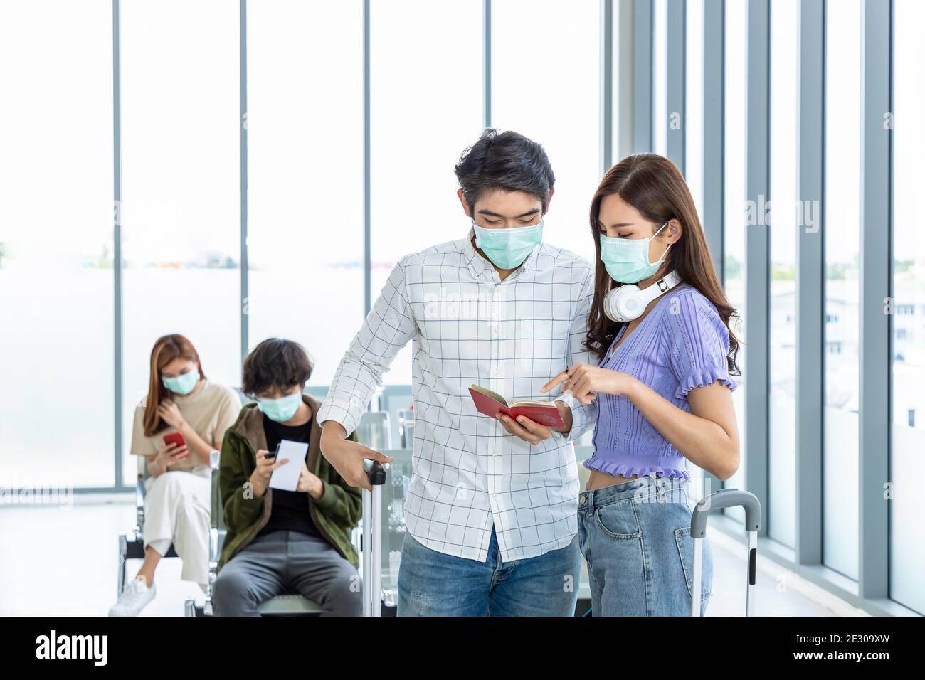 Coppie di viaggiatori che indossano una maschera protettiva in aeroporto, durante la pandemia di Covid-19, con protocollo di allontanamento sociale. Tenendo in mano e indicando il passaporto e d Foto Stock