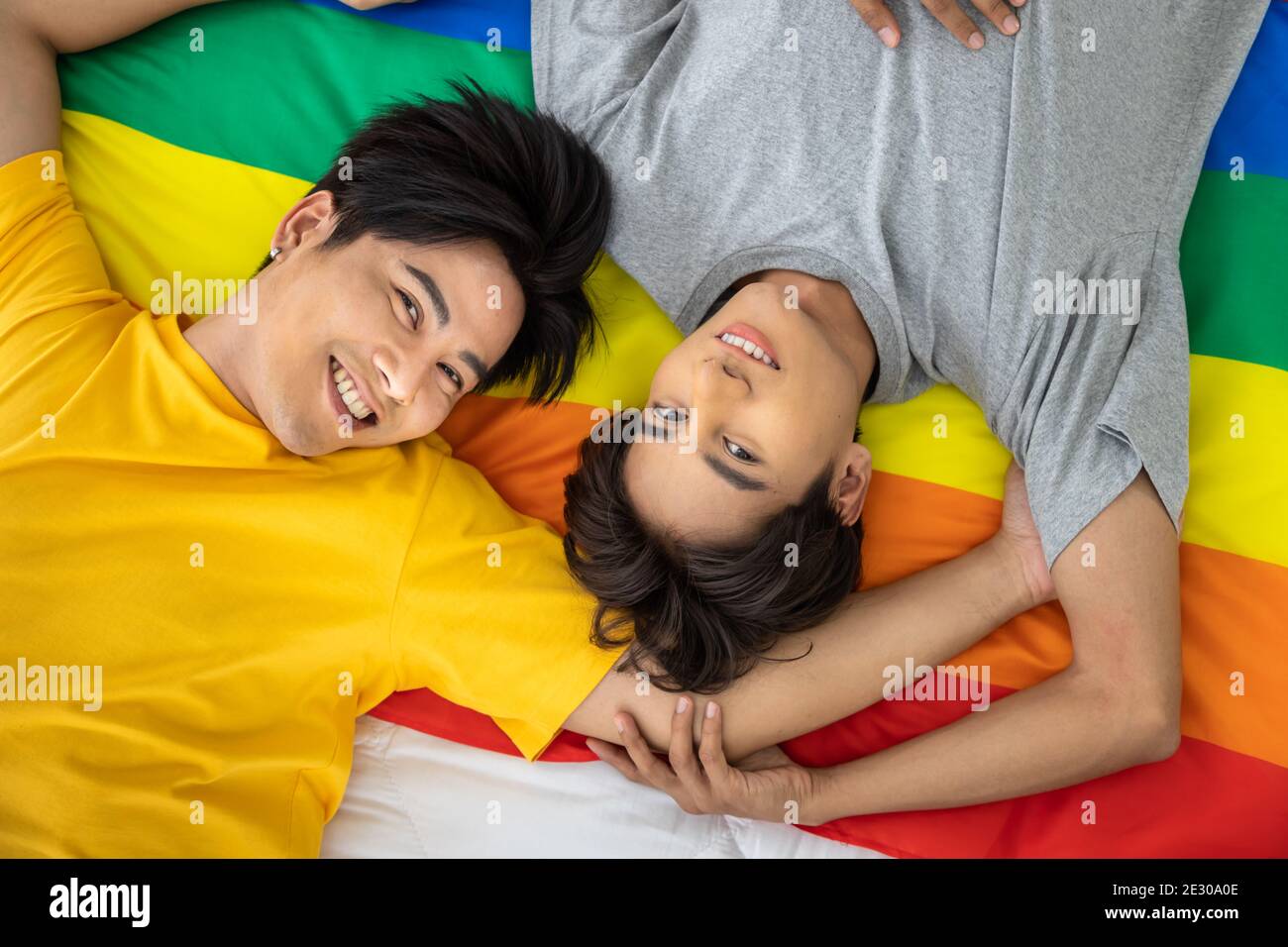 Felice coppia omosessuale asiatica che giace sulla bandiera di orgoglio arcobaleno. Concetto LGBT. Guardando la fotocamera. Foto Stock