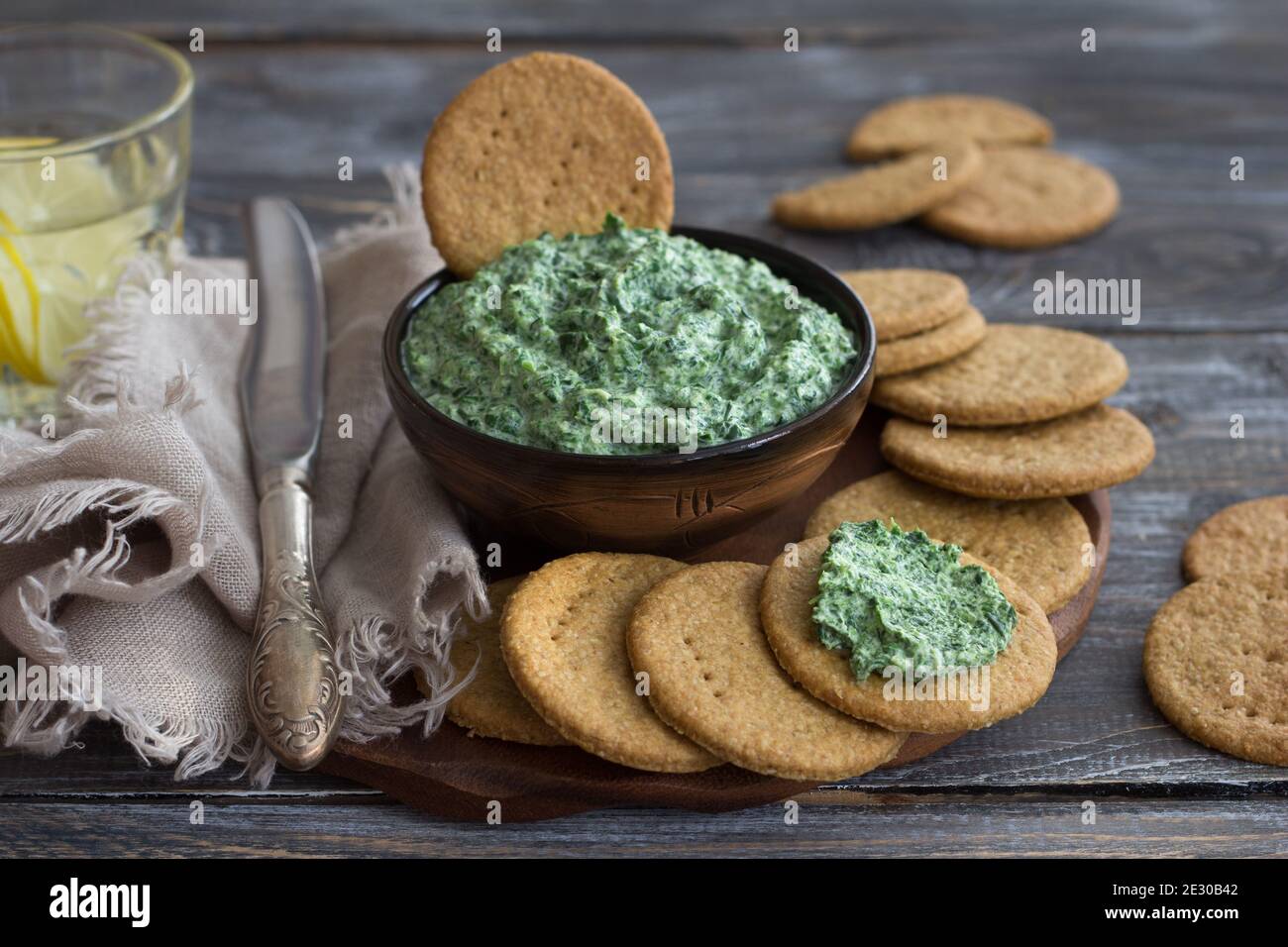 Gli spinaci verdi si immergono con formaggio cremoso, aglio e spezie su una tavola di legno con cracker di avena, stile rustico, fuoco selettivo. Cibo sano fatto in casa Foto Stock