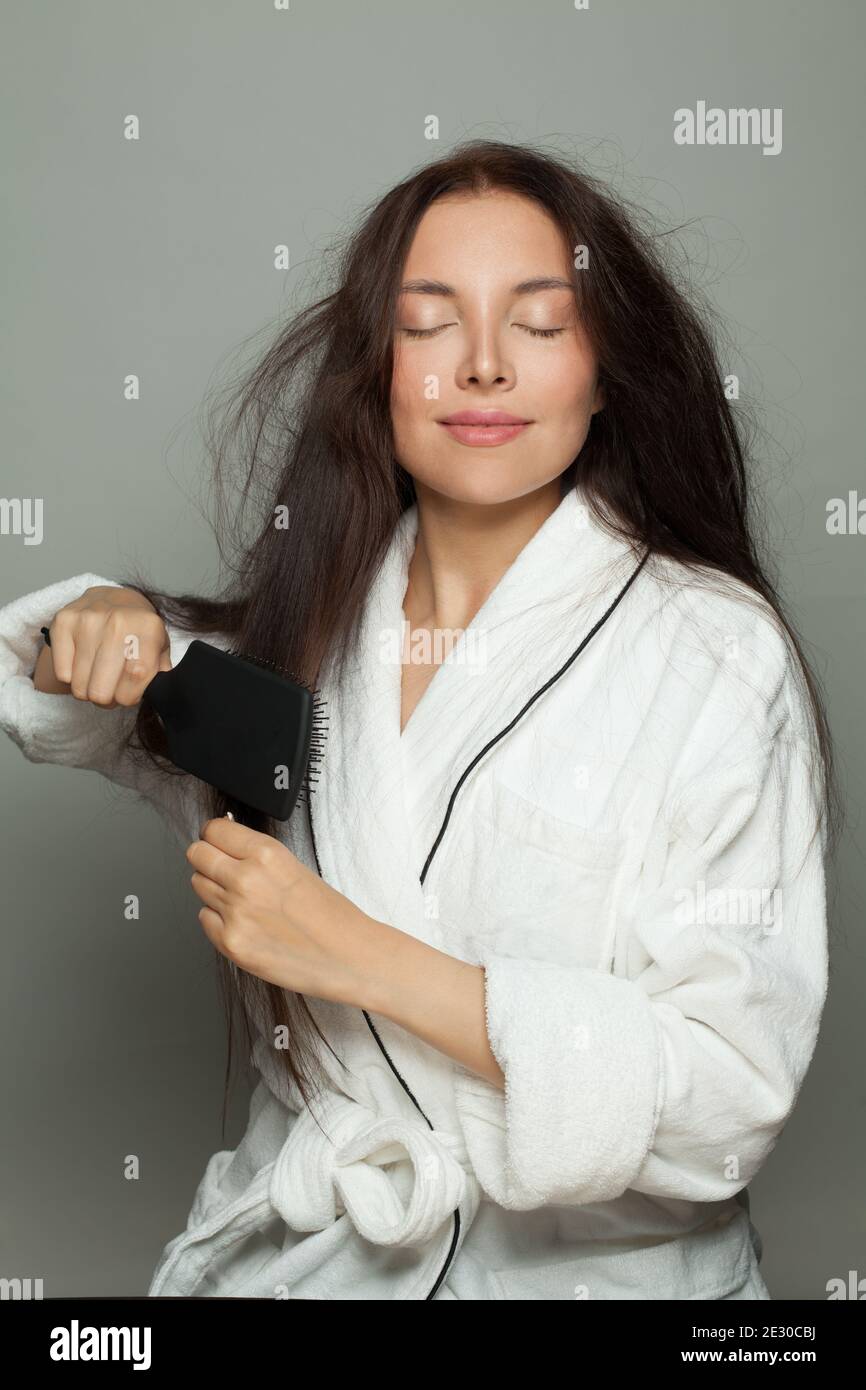 Donna bruna felice che combatte i suoi capelli aggrovigliati su sfondo bianco Foto Stock