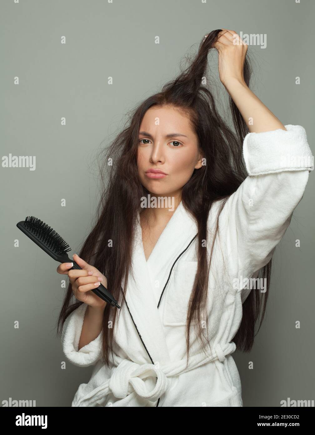 Donna triste con capelli aggrovigliati che tengono il pettine su sfondo bianco. Cura dei capelli e concetto di problema dei capelli Foto Stock