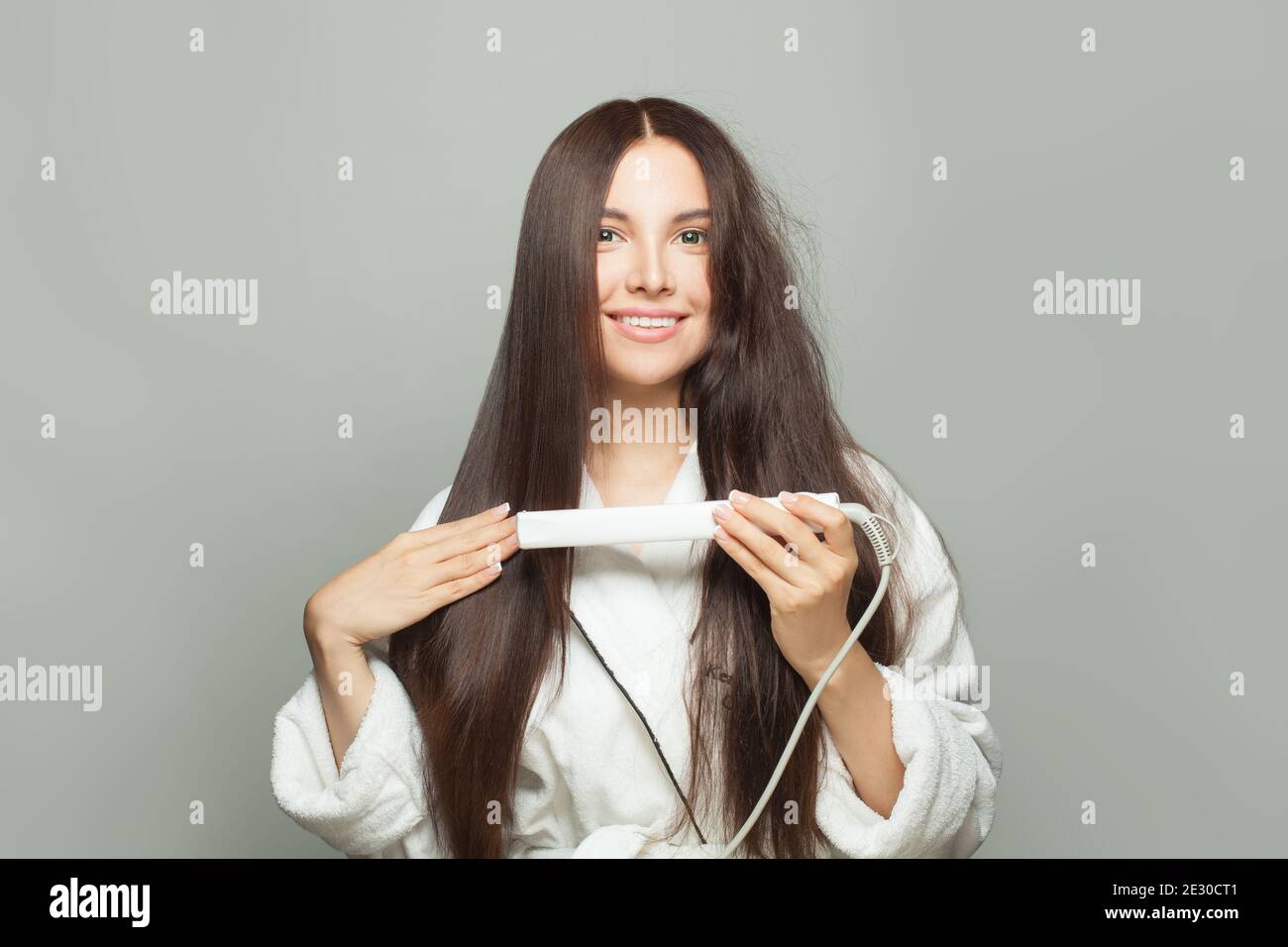 Donna sana bruna raddrizza i capelli con la piastra su sfondo bianco. Concetto di cura dei capelli Foto Stock
