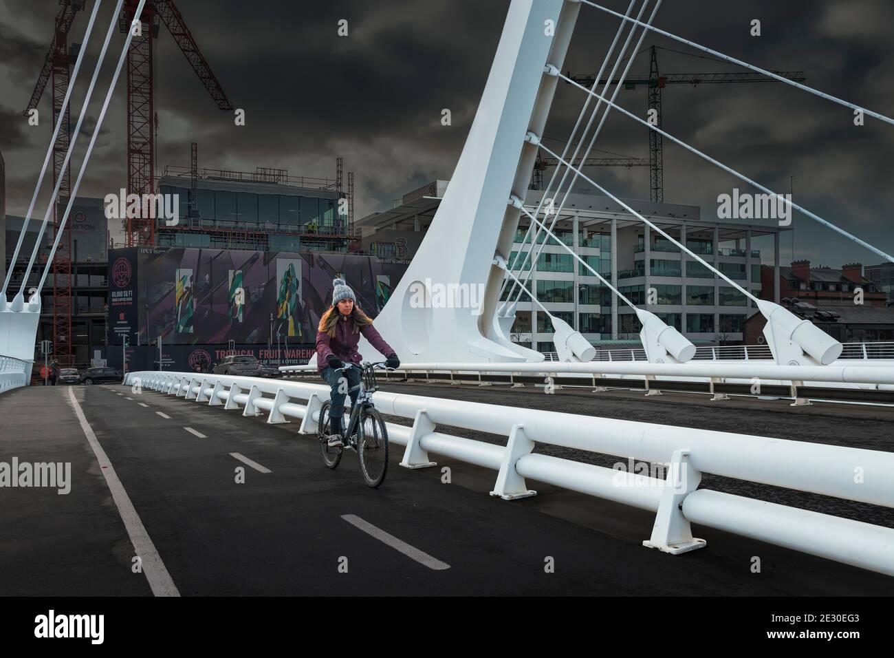 Giovane donna che corre in bicicletta sulla pista ciclabile del Ponte di Arpa (Samuel Beckett Bridge). Dublino. Irlanda. Foto Stock