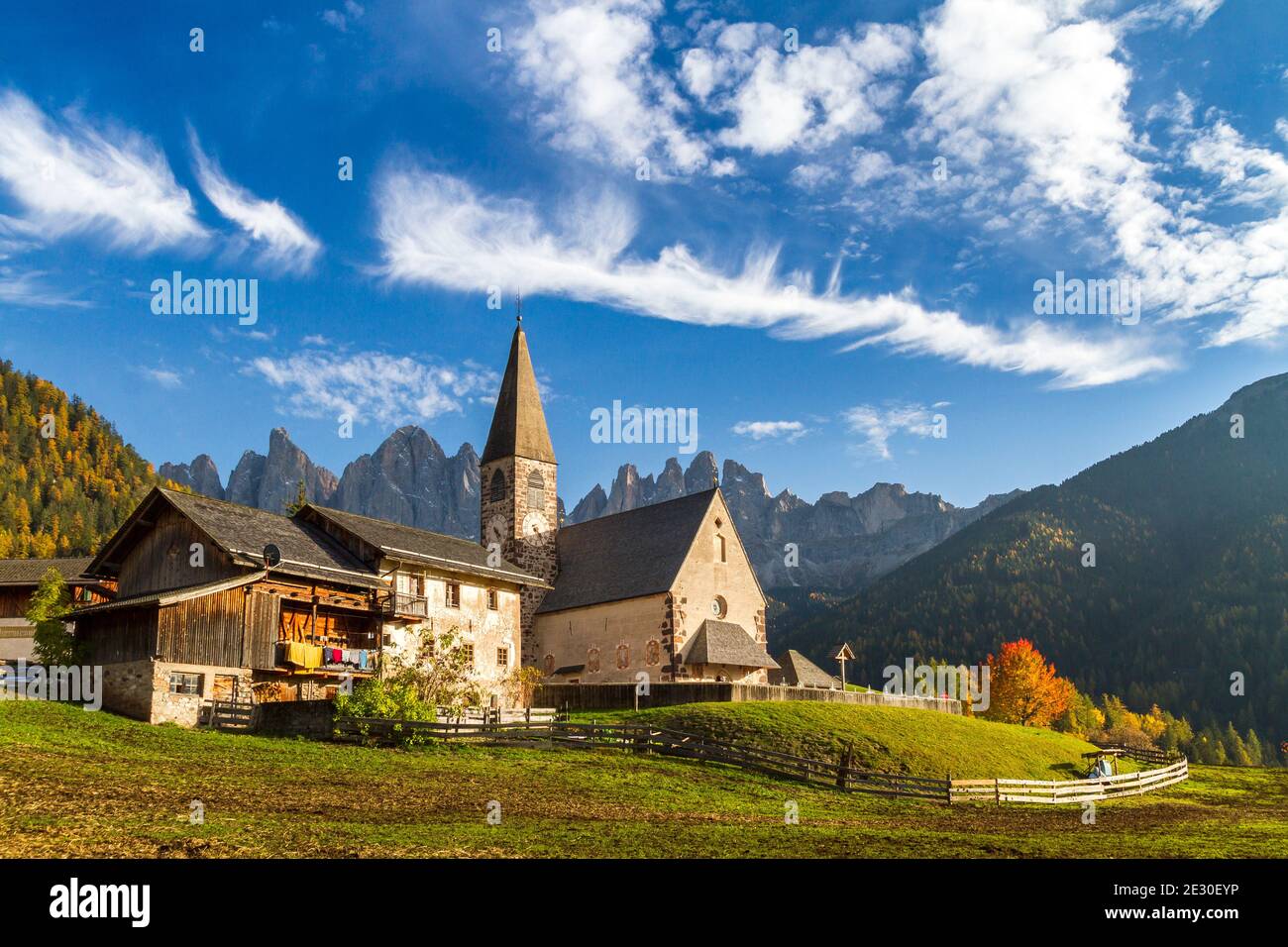 Vista della caratteristica chiesa e della città di San Magdalena con l'Odle sullo sfondo. Val di Funes, Alpi Dolomiti, Trentino Alto Adige, Italia. Foto Stock