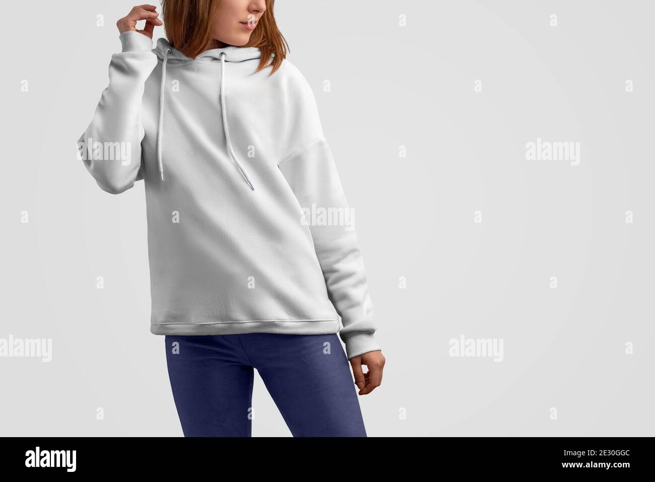 Serie di abiti mockup. Donna caucasica gracile in una felpa bianca con cappuccio e pantaloni blu isolati sullo sfondo vuoto dello studio. Posa frontale. Modello CAN u Foto Stock