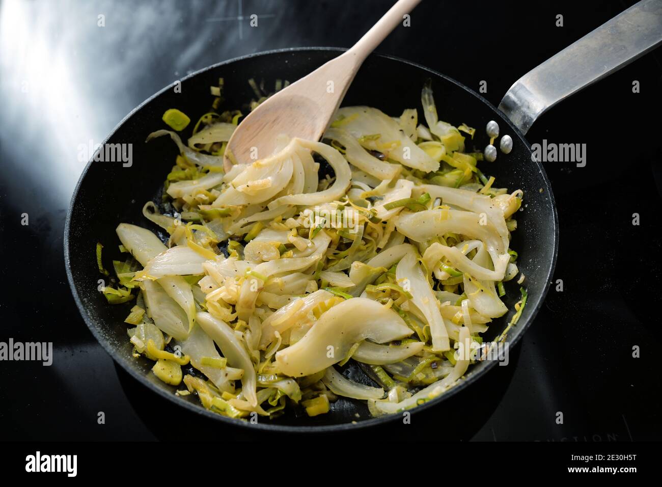 Fette di finocchio e porri in una padella nera sulla stufa, cucina vegetariana con verdure sane, fuoco selezionato, profondità di campo stretta Foto Stock