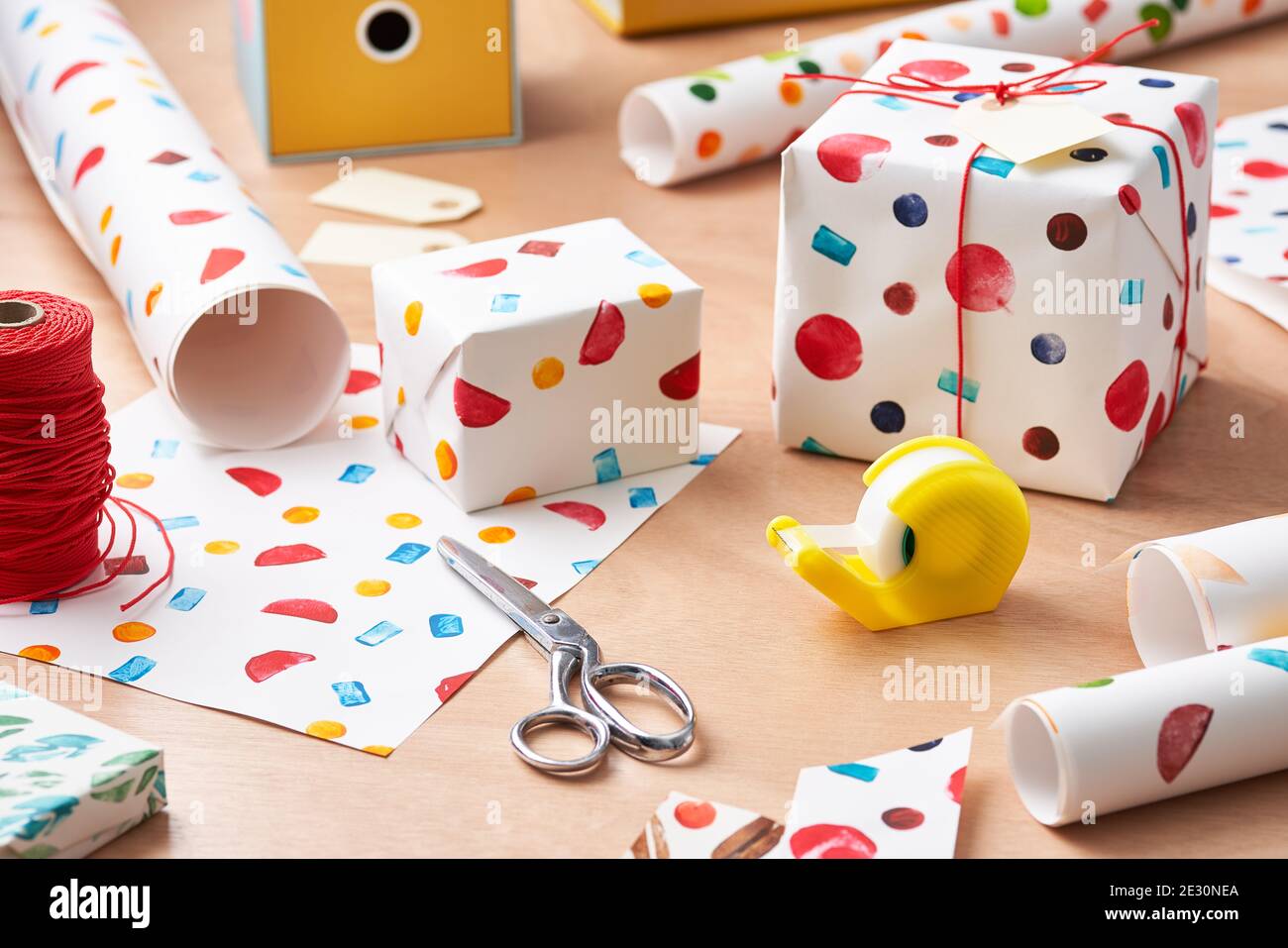 Forbici e nastro adesivo posizionati sul tavolo vicino alle confezioni regalo con un rivestimento creativo fatto a mano Foto Stock