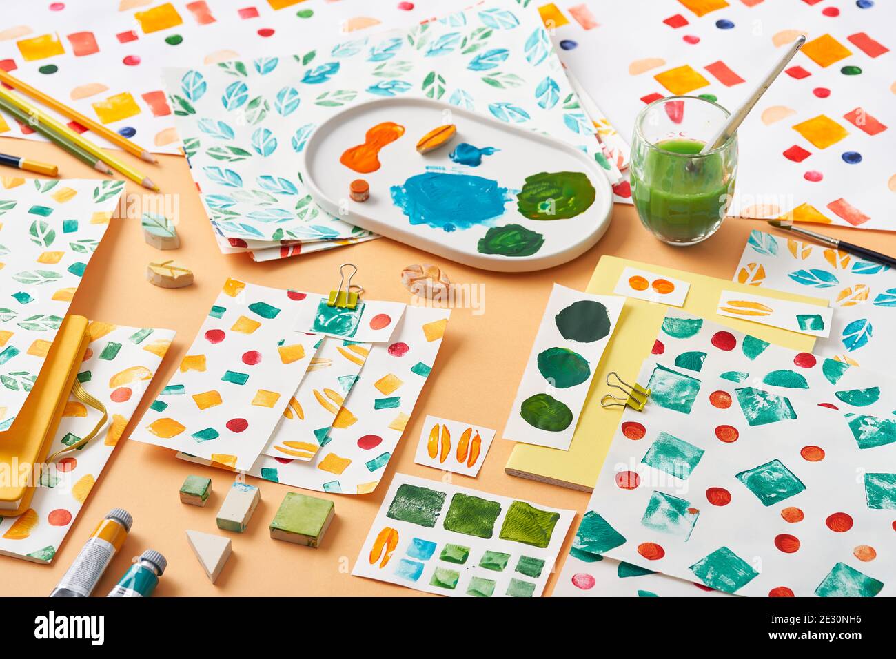 Fogli di carta con vari ornamenti geometrici e campioni posti vicino agli strumenti di tavolozza e pittura su sfondo arancione Foto Stock