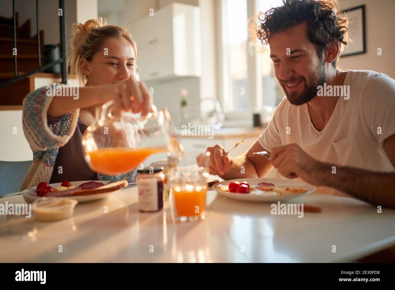 Una giovane e felice coppia ama gustare un succo d'arancia fresco per la colazione anche in una bella giornata di sole a casa. Rapporto, amore, insieme, colazione Foto Stock