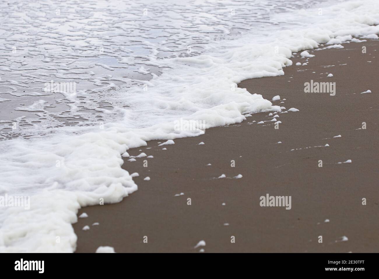 primo piano di linea del mare con schiuma, acqua schiumosa presso la spiaggia di sabbia nera Foto Stock